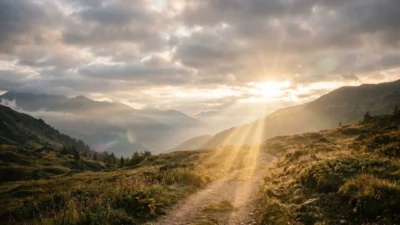 Sunbeams breaking through morning clouds over a scenic winding path in lush mountain foothills.